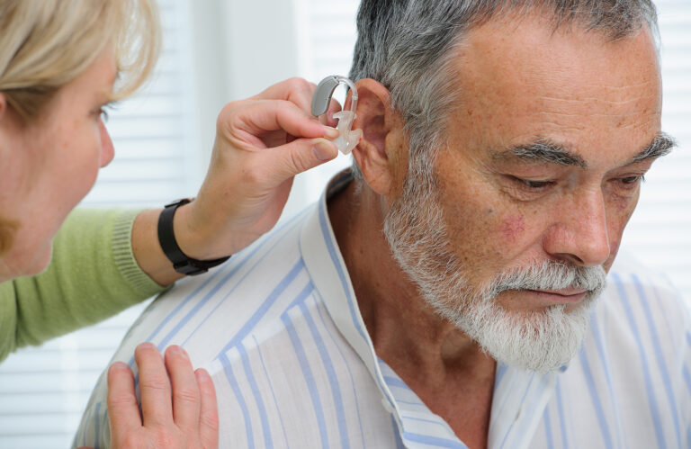 private hearing aids - Doctor inserting hearing aid in senior's ear
